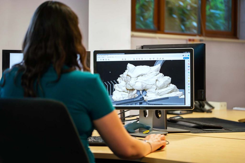Fiatal nő ellenőriz egy 3D-s látványtervet egy készülő játék számára. A képernyőjén egy hullámvasút részlete látható, aminek a sínje átfut egy oroszlán száját formázó kapun.