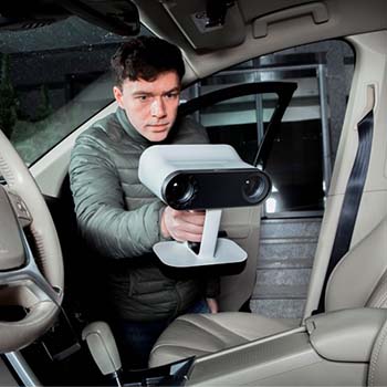 Szürkészöld kabátos fiatalember digitalizálja egy autó belsejét az Artec Leo kéziszkennerével.